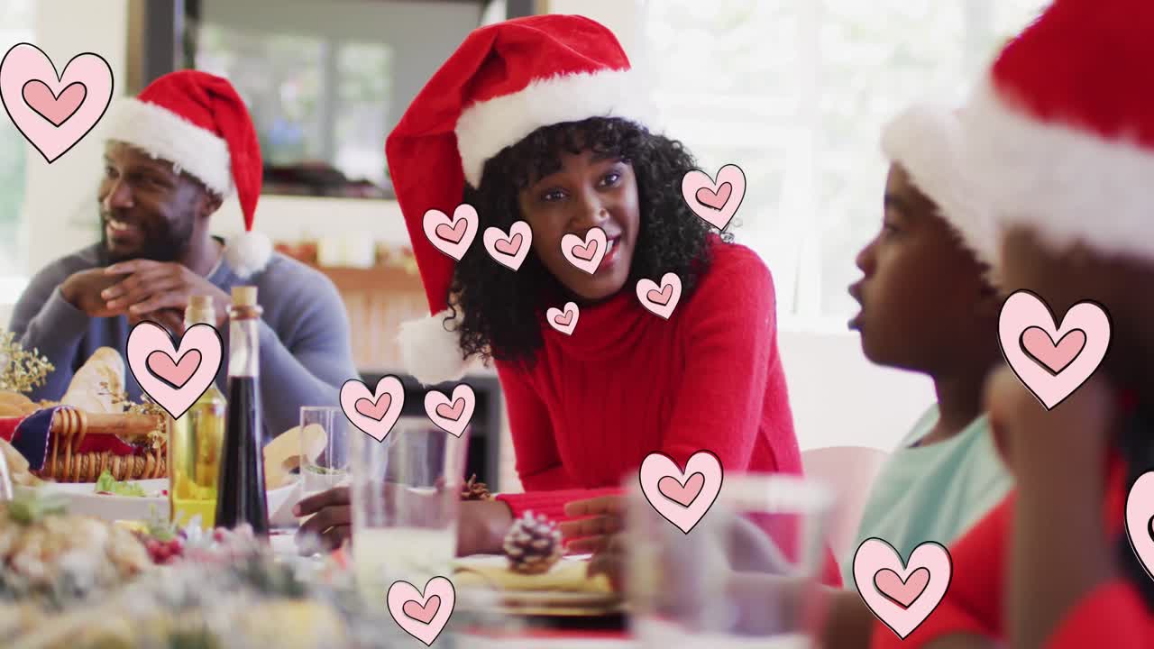 animación de corazones flotando sobre una feliz familia afroamericana durante la cena de navidad
