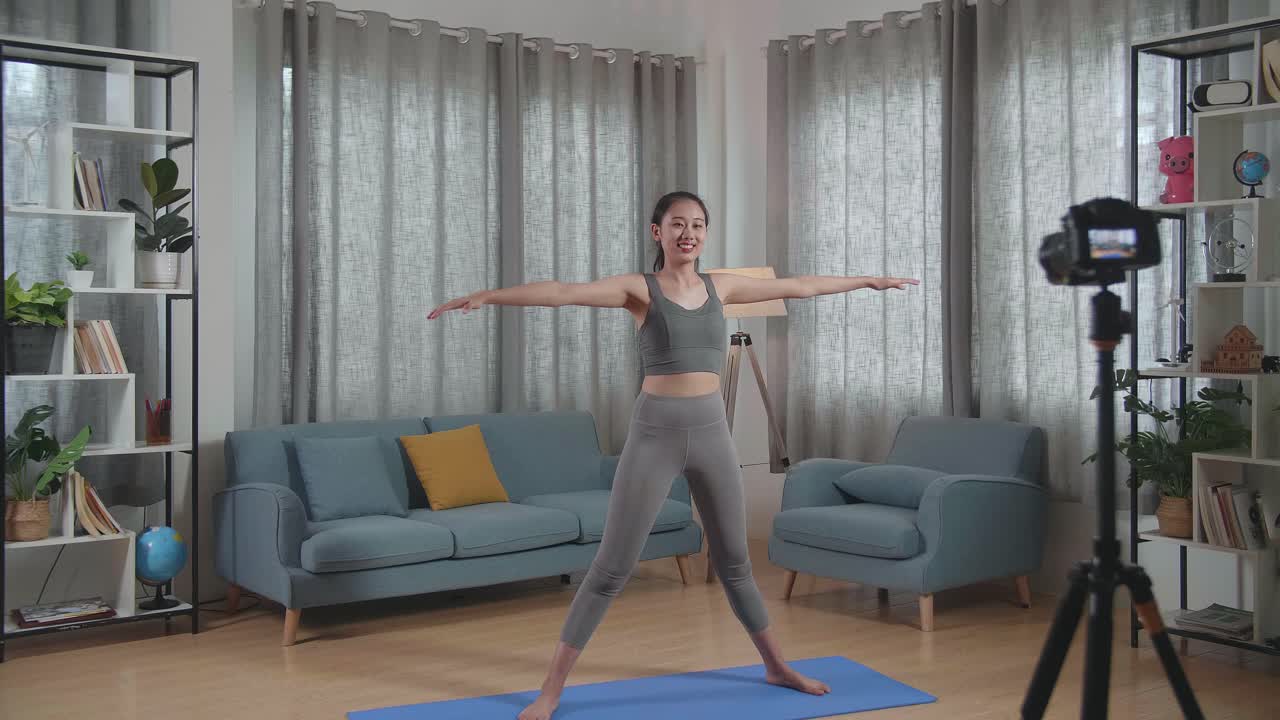 젊은 아시아 트레이너 여성 스포츠 옷을 입고 카메라에 대화하고 집에서 운동을 가르치는 동안 스트레칭