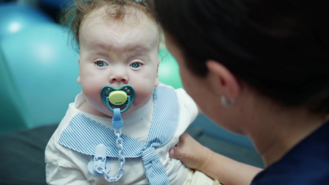 Infant client receiving professional pediatric therapy, a physiotherapist holding a baby in a medical environment with colorful objects