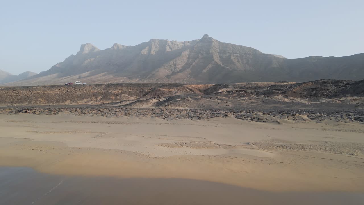 Aerial drone shot flying forward over the ocean at sunset near Cofete Beach, Fuerteventura — calm waves, golden light, and open horizon.