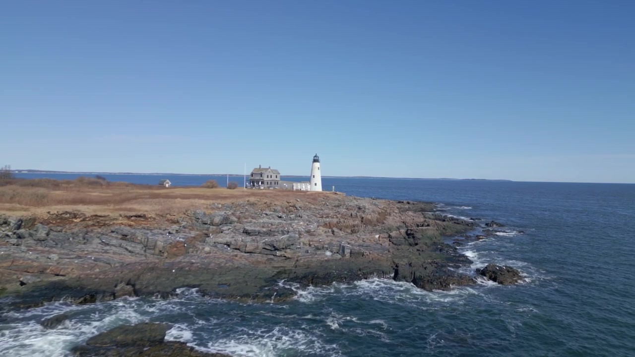Luftfoto af fyrtårn og hus ved New Hampshires kystlinje med klippekyster og åbent hav.