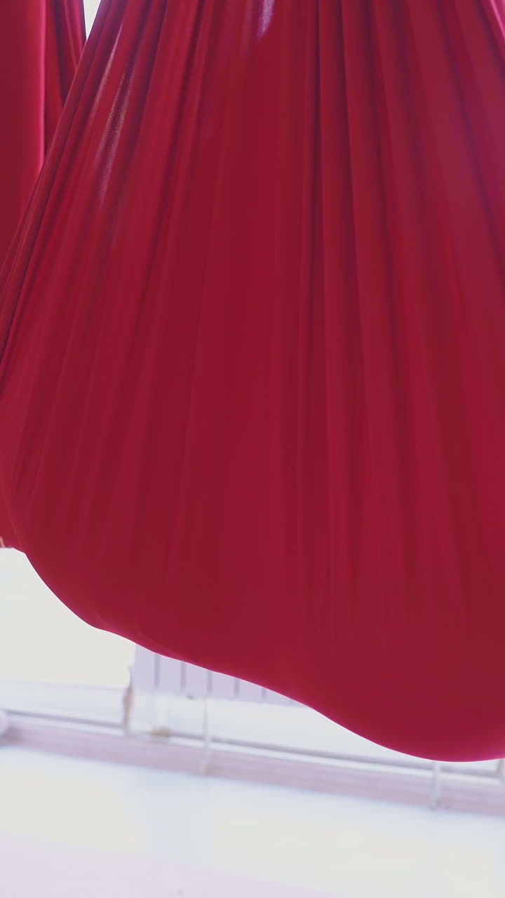 red aerial fly yoga hammocks support relaxed women bodies with stretched legs in bright leggings close view