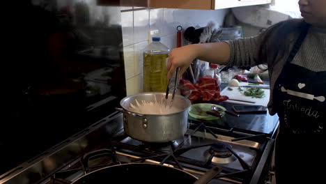 female chef stirring raw spaghetti noodles inside large pot with hot water on cooker inside kitchen