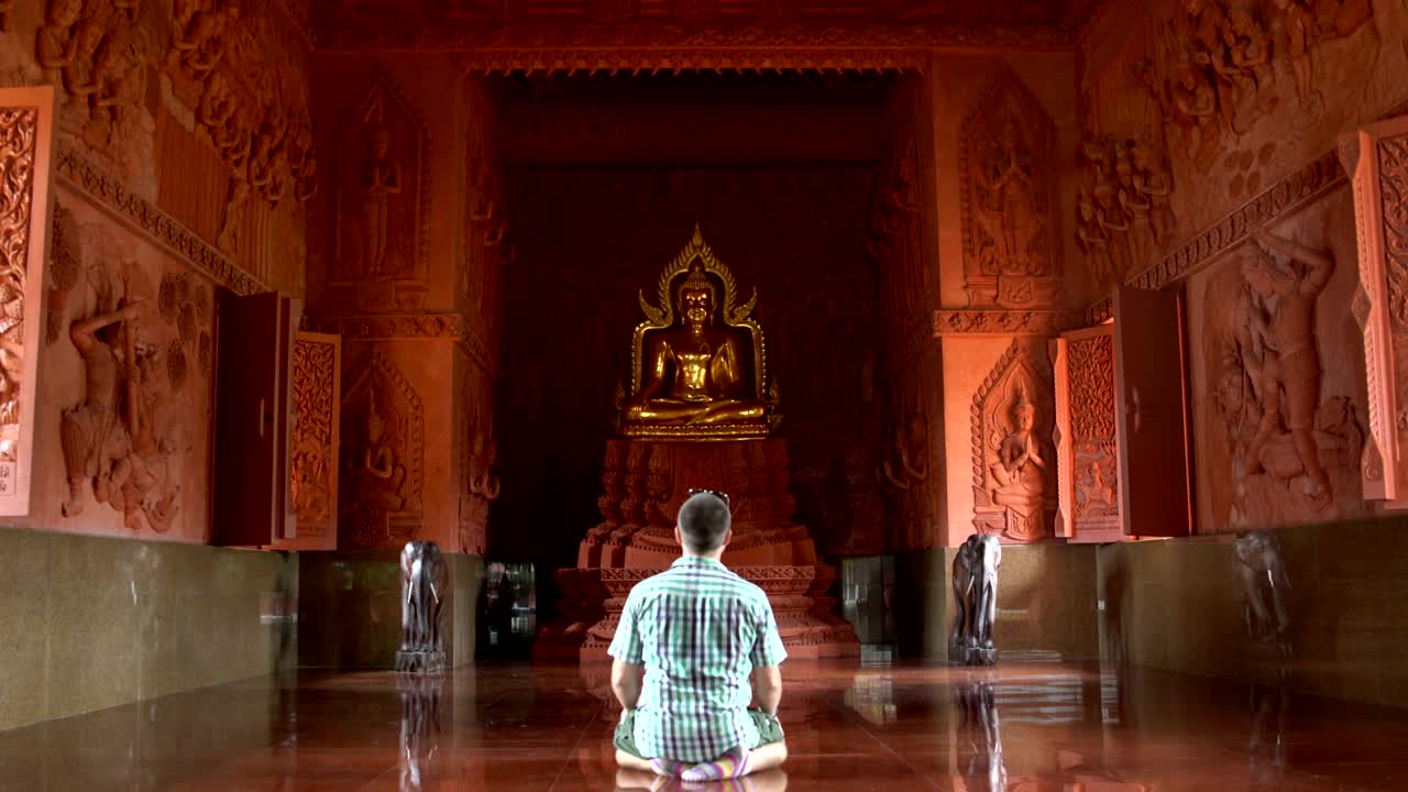 A man prays kneeling in front of a Buddha statue in a Buddhist temple