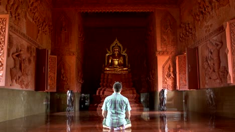 un hombre reza arrodillado frente a una estatua de buda en un templo budista