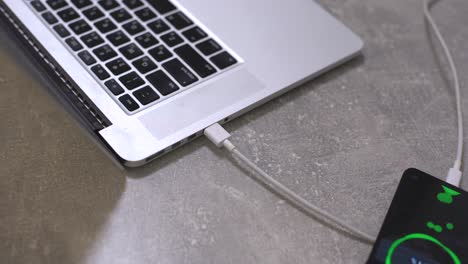 mano enchufando el cargador en el teléfono celular contra el ordenador portátil