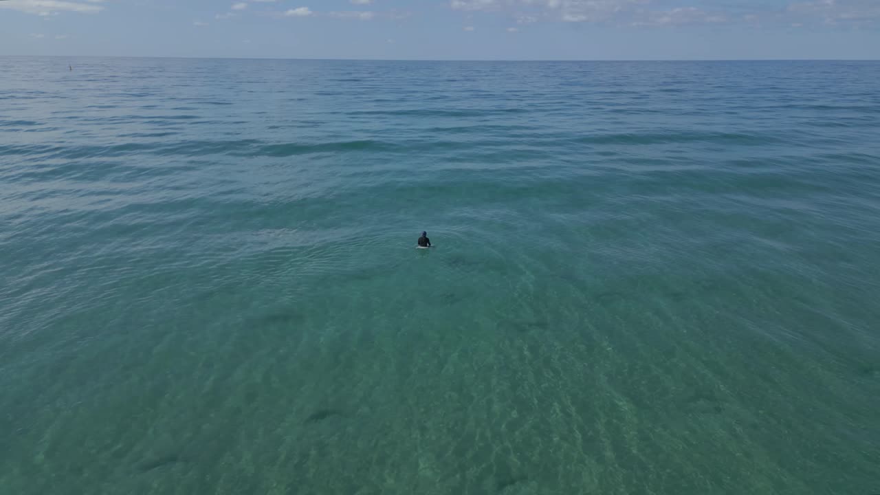 4k drone of lone surfer sitting out in the blue green waters off Gold Coast beach in Australia
