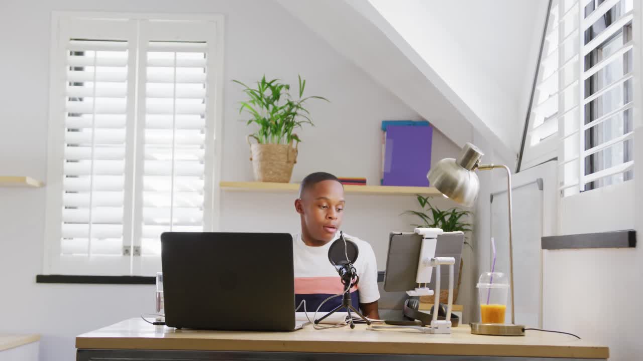 menino adolescente afro-americano feliz gravando podcast usando laptop, câmera lenta
