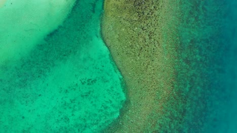 Beautiful-sea-texture-with-corals-and-rocks-under-calm-clear-emerald-water-of-shallow-turquoise-lagoon-near-white-sandy-beach,-Thailand