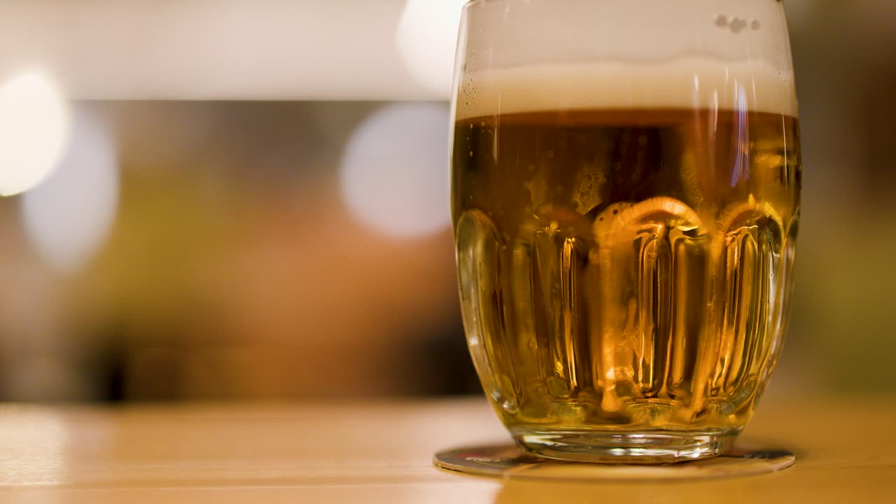 A foamy lager is placed beside another glass on a wooden table in a brewpub