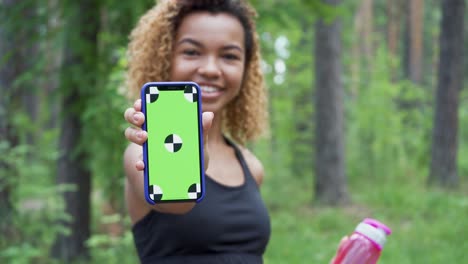 black young woman using her smartphone after jogging and shows green screen to the camera