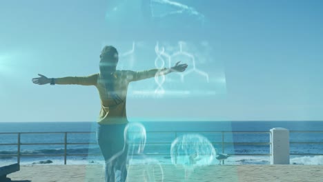 Animation-of-screens-floating-over-woman-walking-on-promenade-by-the-sea