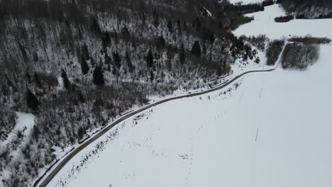 Car-driving-through-the-road-between-forest-and-valley-covered-in-thick-snow