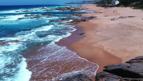 Aerial-shot-of-a-coastline-where-the-ocean-meets-the-shore-pan-down