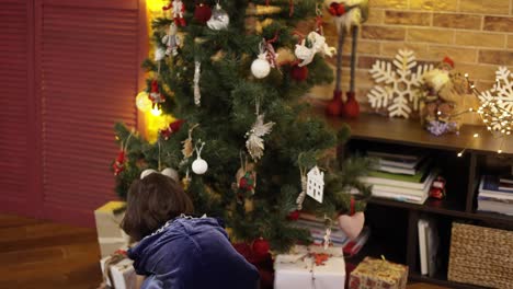 niña feliz colocando una caja de regalo debajo del árbol de navidad decorado