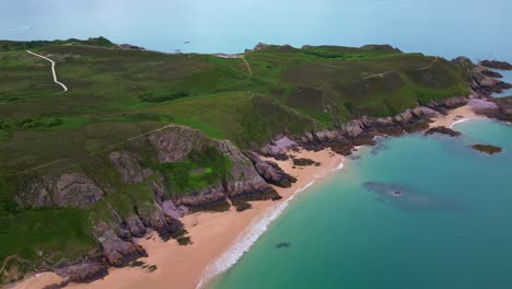 drone flies backward along erquy’s coast, revealing sandy beach, rocky cliffs, hiking paths and turquoise sea. brittany, france