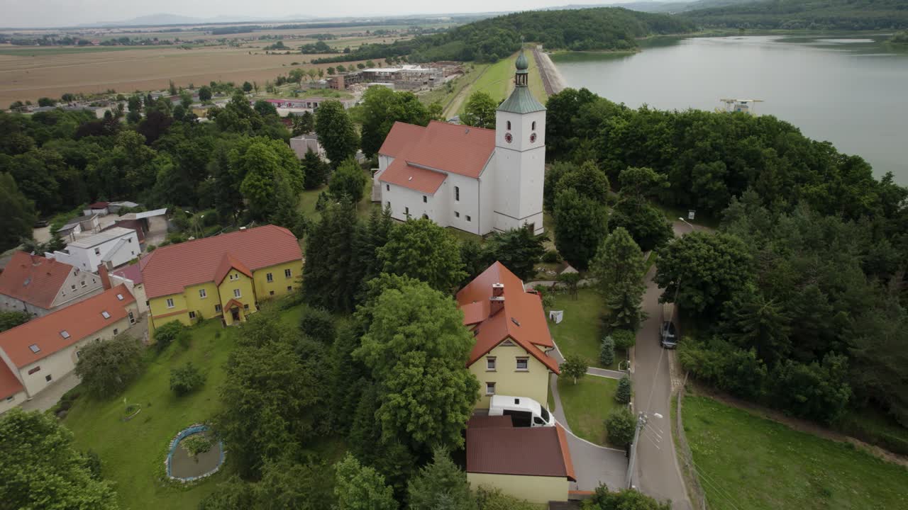 Orbita aerea ravvicinata sopra una vecchia chiesa situata sulla collina, sopra la diga d'acqua.