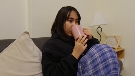 beautiful filipino girl curled up and staring with mug on sofa