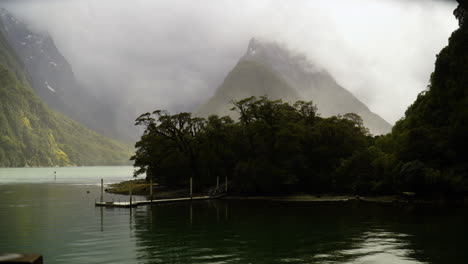 niebla y nubes alrededor del pico mitre en milford sound, fiordland, nueva zelanda con un pequeño puerto en primer plano
