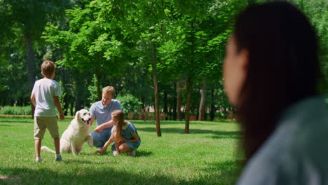 Frau-Beobachtet-Familie-Beim-Spielen-Mit-Hund-Im-Park,-Verschwommene-Sicht.-Aktives-Lebenskonzept.