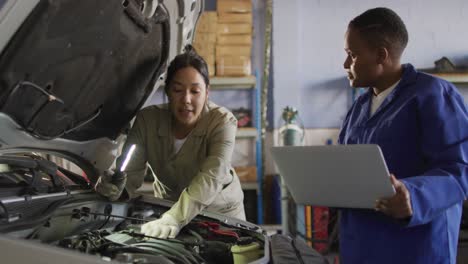 Video-of-two-diverse-female-car-mechanics-talking,-using-laptop-and-repairing-car