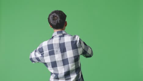 back view of young asian teen boy holding a microphone and rapping on the the green screen background