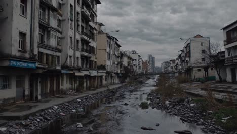 murky water coursing through concrete canal, surrounded by deteriorating urban structures under overcast sky, revealing environmental neglect and urban decay