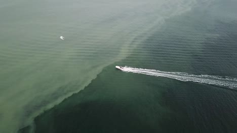 motorboat sailing swiftly across the silty sea water - aerial drone