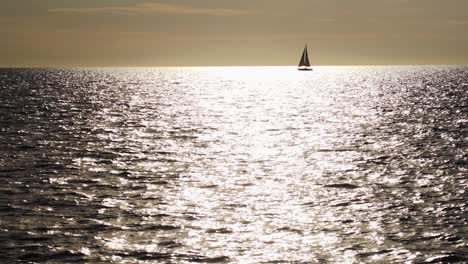 toma en cámara lenta de la silueta del velero pasando por el reflejo del sol en el agua