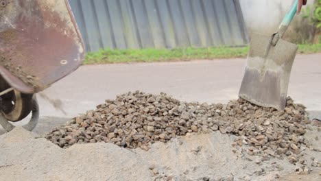 dumping rocks gravel into the cement mixture from the wheelbarrow to create a concrete mixture in the streets