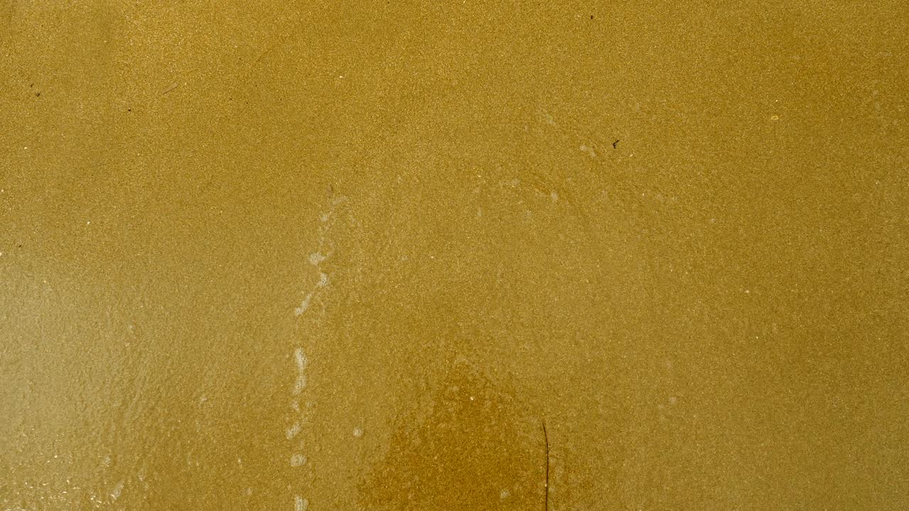 emoji. vista superior de la ola que lava el rostro triste dibujado en la arena de la playa de arena del mar mediterráneo. 4k