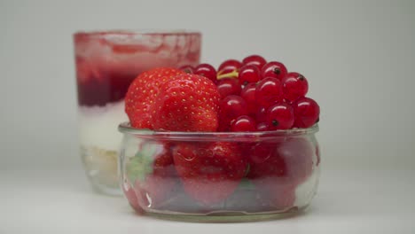 a delectable strawberry shortcake in a glass and a few strawberries and red currants on a clear bowl - close up shot