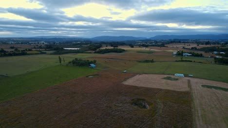 Dolly-in-flyover-of-some-natural-fields,-some-part-of-burnt-brown-color-in-the-nature-of-Chiloe,-Chile-on-a-cloudy-day,-mountainous-skyline