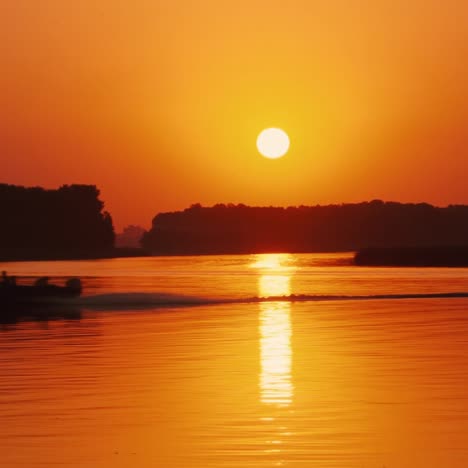 silhouettes of people in a motor boat sailing along the river at sunset