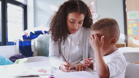 Female-infant-school-teacher-working-one-on-one-with-a-young-black-schoolboy,-close-up