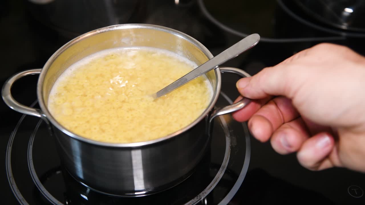 Mano maschile che mescola la zuppa nella pentola e la sposta dal fornello della cucina, cucinando spaghetti tradizionali per zuppa, primo piano, nessuno