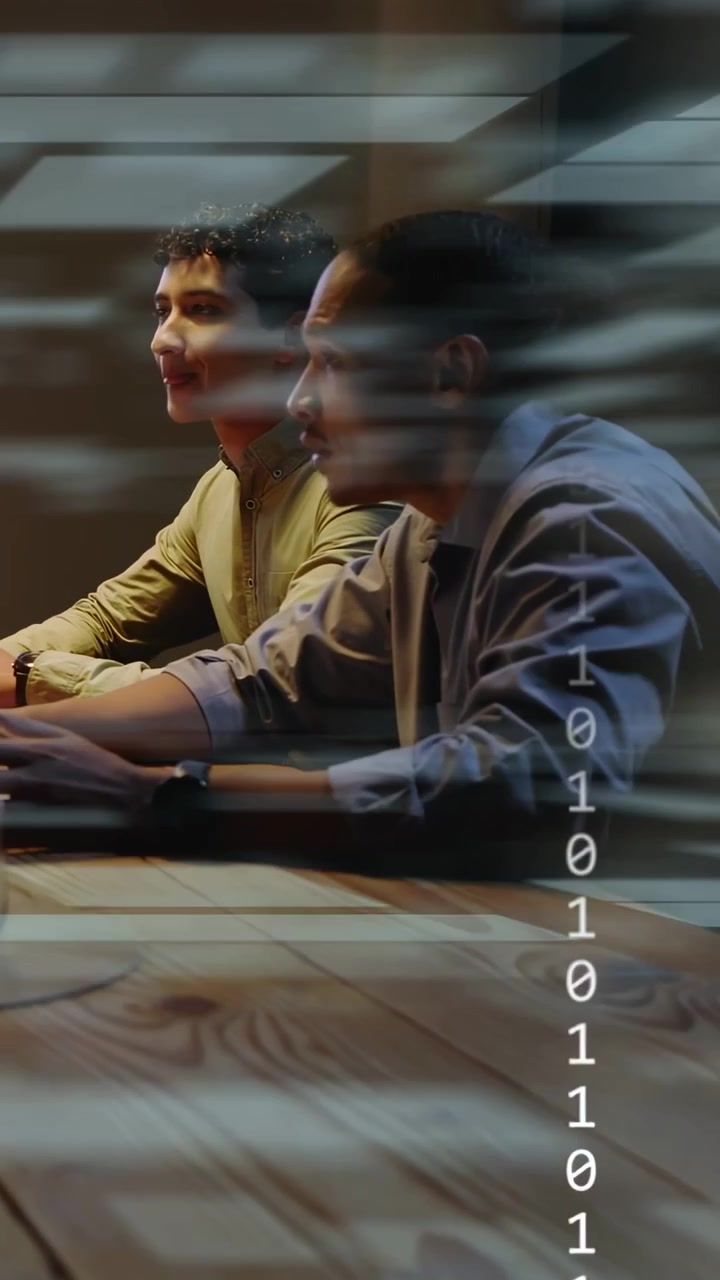 Vertical video: Dev typing at table, causing tech binary overlay while peer turning to speak to fix