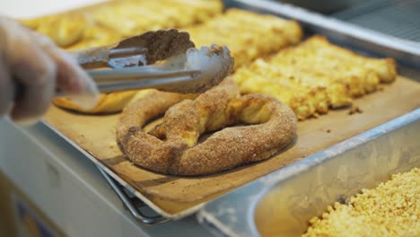 person placing cinnamon sugar soft pretzel on a tray with other freshly baked breads in pastry kitchen - close up, slow motion