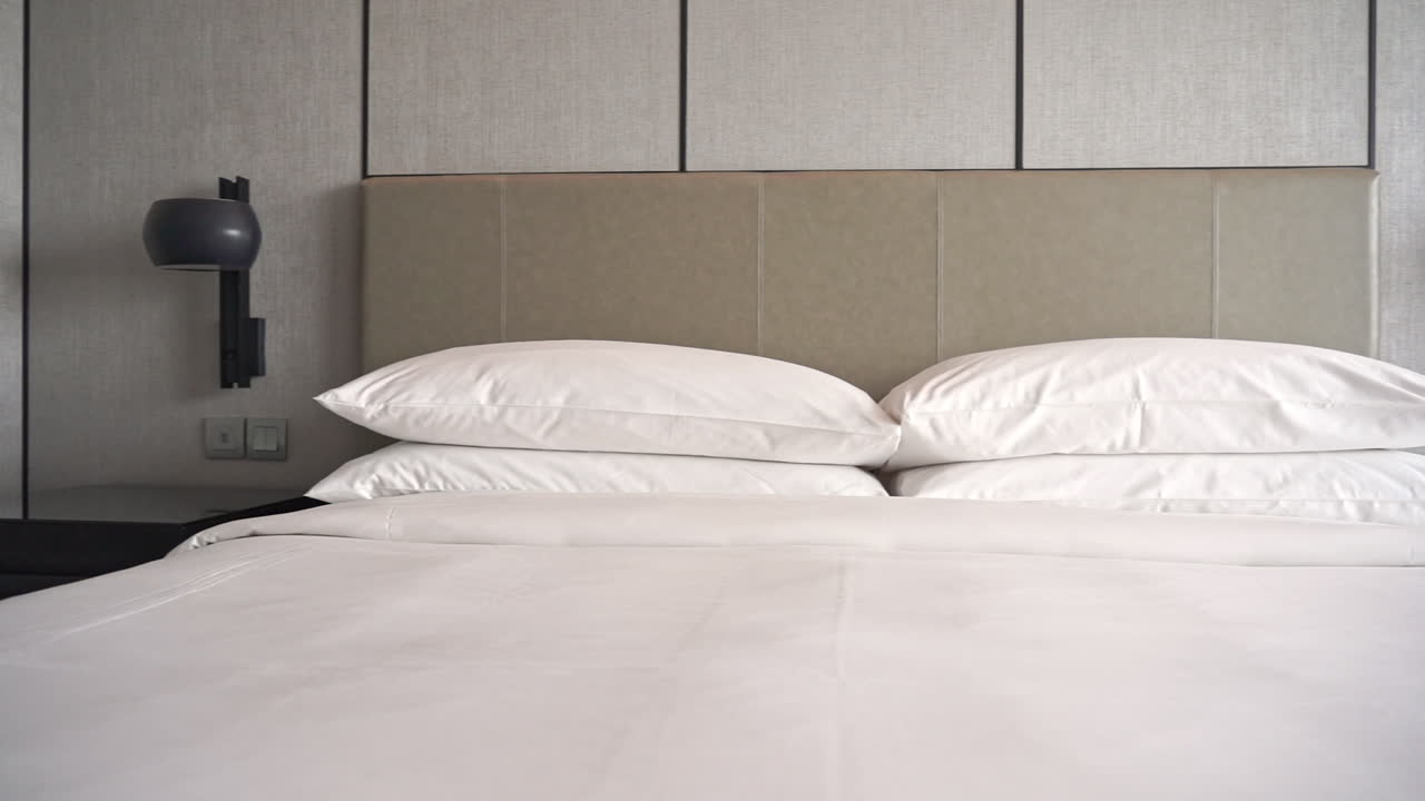 Pan across a hotel bed made up in pure white lined