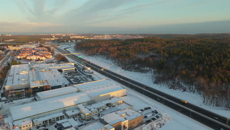 cars driving through the asphalt road along the forest and buildings during winter in dabrowa, gdynia