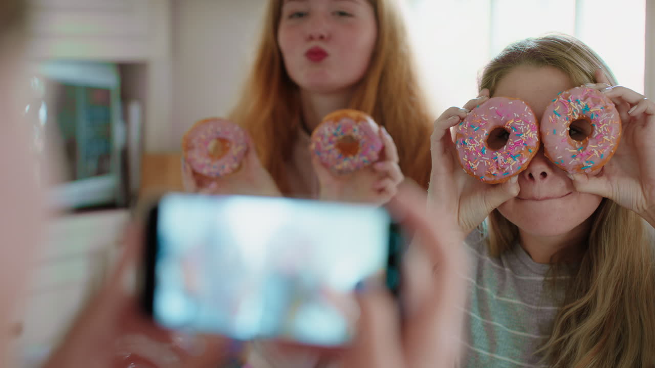 chicas adolescentes divertidas posando con rosquillas tomando fotos usando teléfonos inteligentes compartiendo en las redes sociales disfrutando de pasar el fin de semana en la cocina