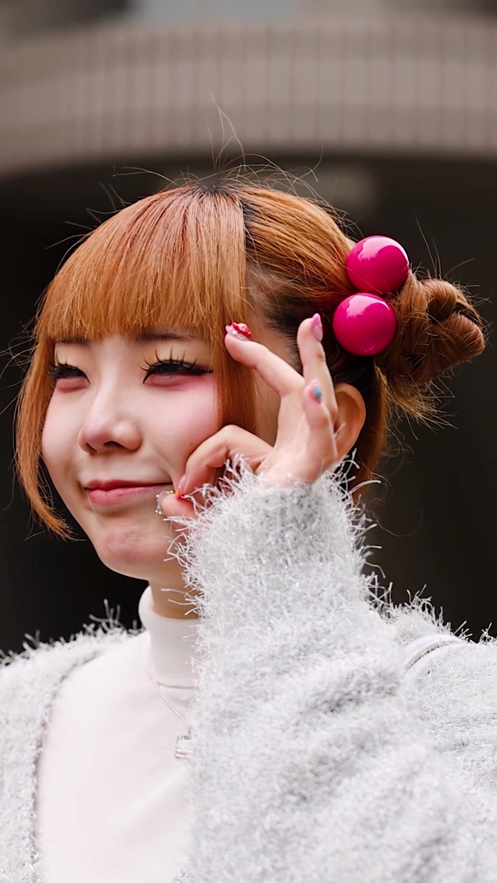 ピンクのヘアアクセサリーをつけた若い女性がカメラに向かってポーズをとる