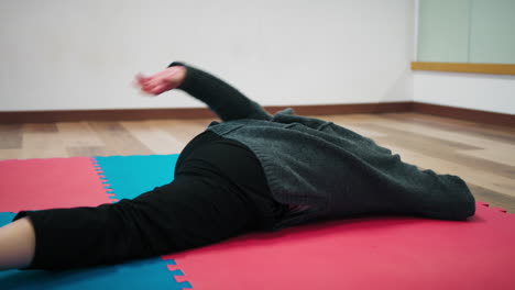 on the tatami of a dance school a woman does stretching pre-dance exercises