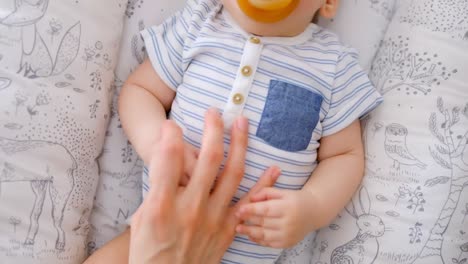 Hand-of-mother-caressing-her-cute-baby-lying-in-the-crib-with-pacifier-4k