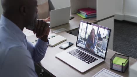 African-american-businessman-sitting-at-desk-using-laptop-having-video-call-with-female-colleague