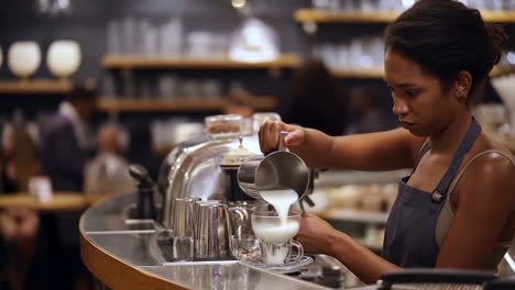 barista prepares a coffee drink by pouring steamed milk into a cup in a cafe