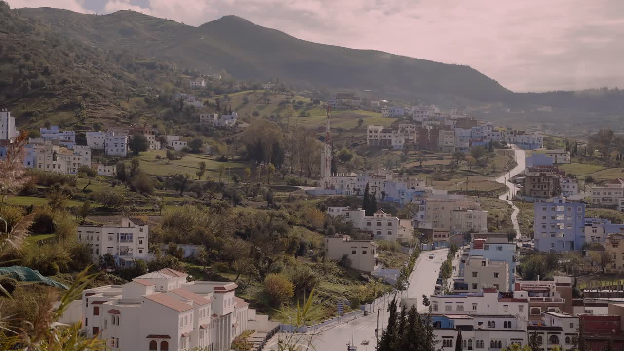 amplia vista de los edificios azules que rodean una carretera que cruza un valle que conduce a la ciudad de chefchaouen en marruecos