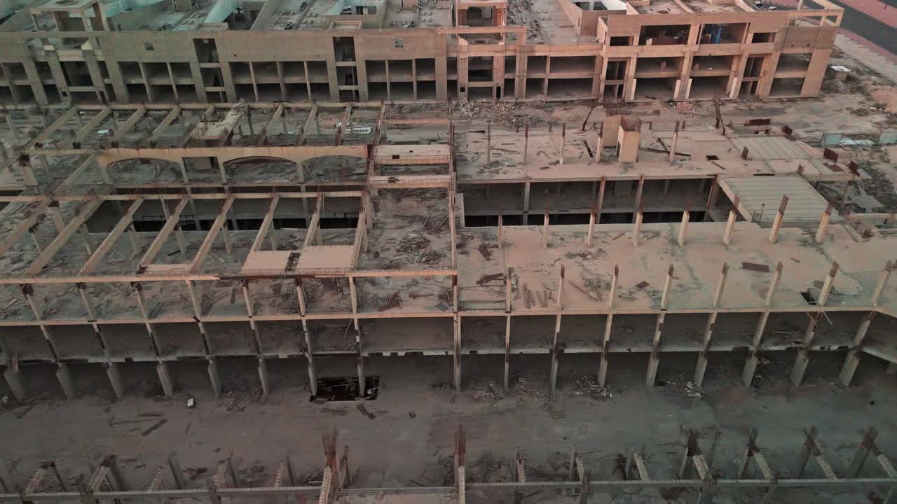 Ripresa aerea con drone di un complesso in cemento abbandonato a più livelli con travi a vista, vani vuoti, macerie sparse e barre di armatura arrugginite: maxiprogetto di costruzione interrotto per temi di degrado urbano, sicurezza e settore immobiliare