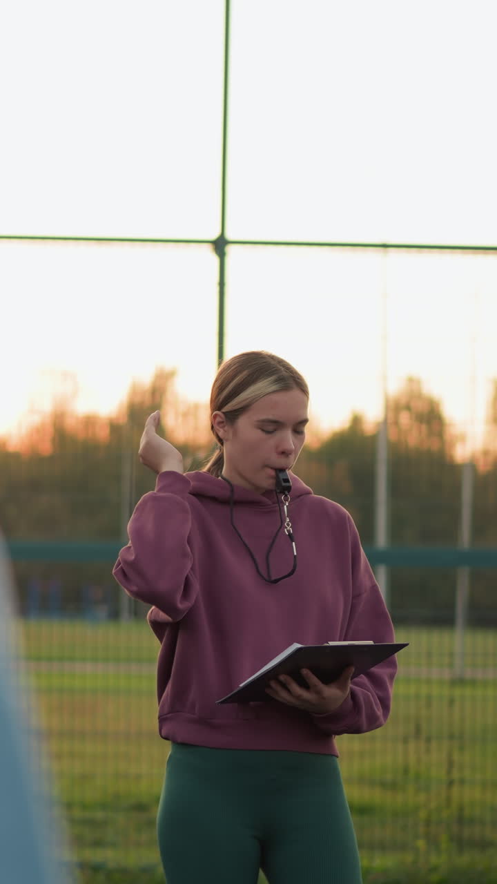 vista trasera de una mujer practicando voleibol con el entrenador observando y tomando notas mientras sostiene un silbato en su boca, el entrenador está centrado en su rendimiento