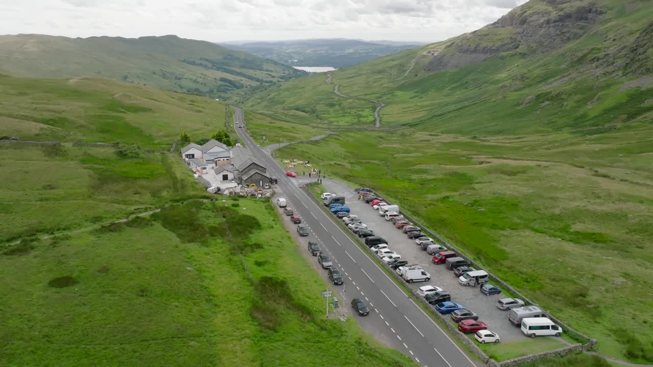 Kirkstone Pass Summit With View Down Towards Lake Windermere. The Kirkstone Pass Inn Next To The A592 And Busy Car Park. Summer. Lake District, Cumbria, UK
